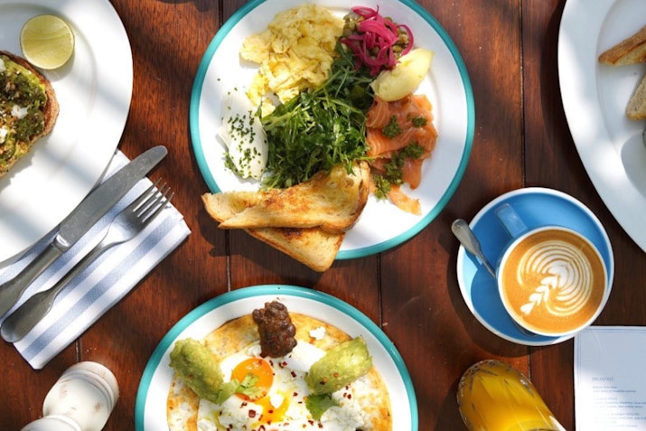 Drool-worthy menu picks: assorted brunch plates with vibrant ingredients and a cappuccino on a wooden table.