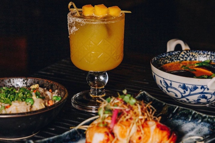 A close-up of colorful pan-Asian dishes and a refreshing drink.