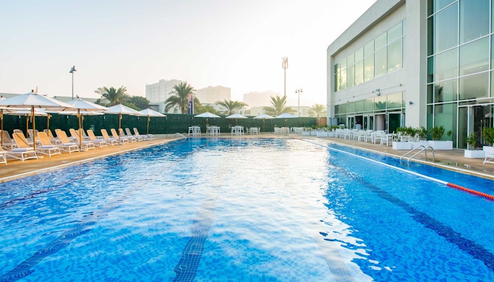 DUBAI Al Furjan Club Swimming pool with lanes, surrounded by lounge chairs and a lifebuoy, with a building in the background.