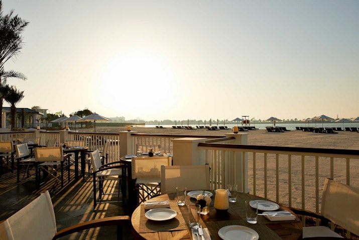 Outdoor dining area overlooking the beach at sunset, set with plates.