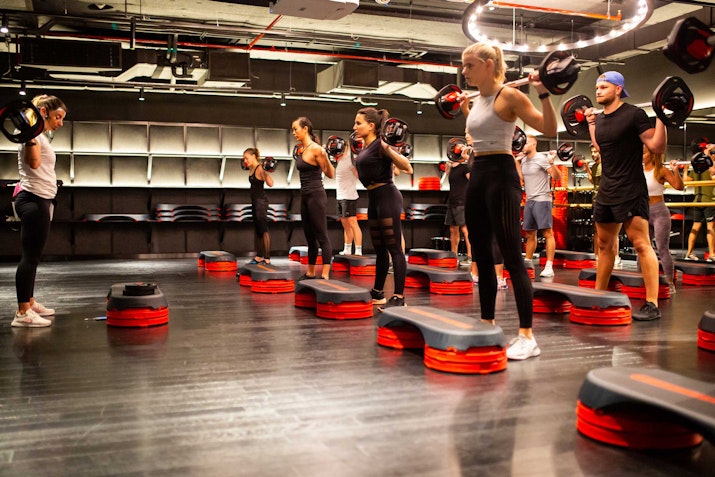 A group of participants in a fitness class lifting weights together in a dynamic workout session.
