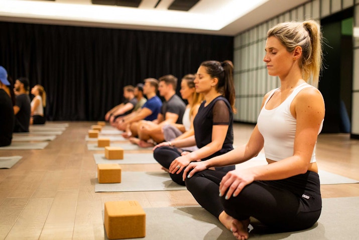 Participants sitting in a meditation pose during a yoga class, focusing quietly with yoga blocks in front of them.