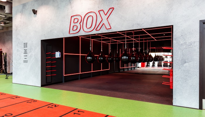 Workout Across 26 Fitness First Locations Boxing area with red and black interior design and hanging punching bags.