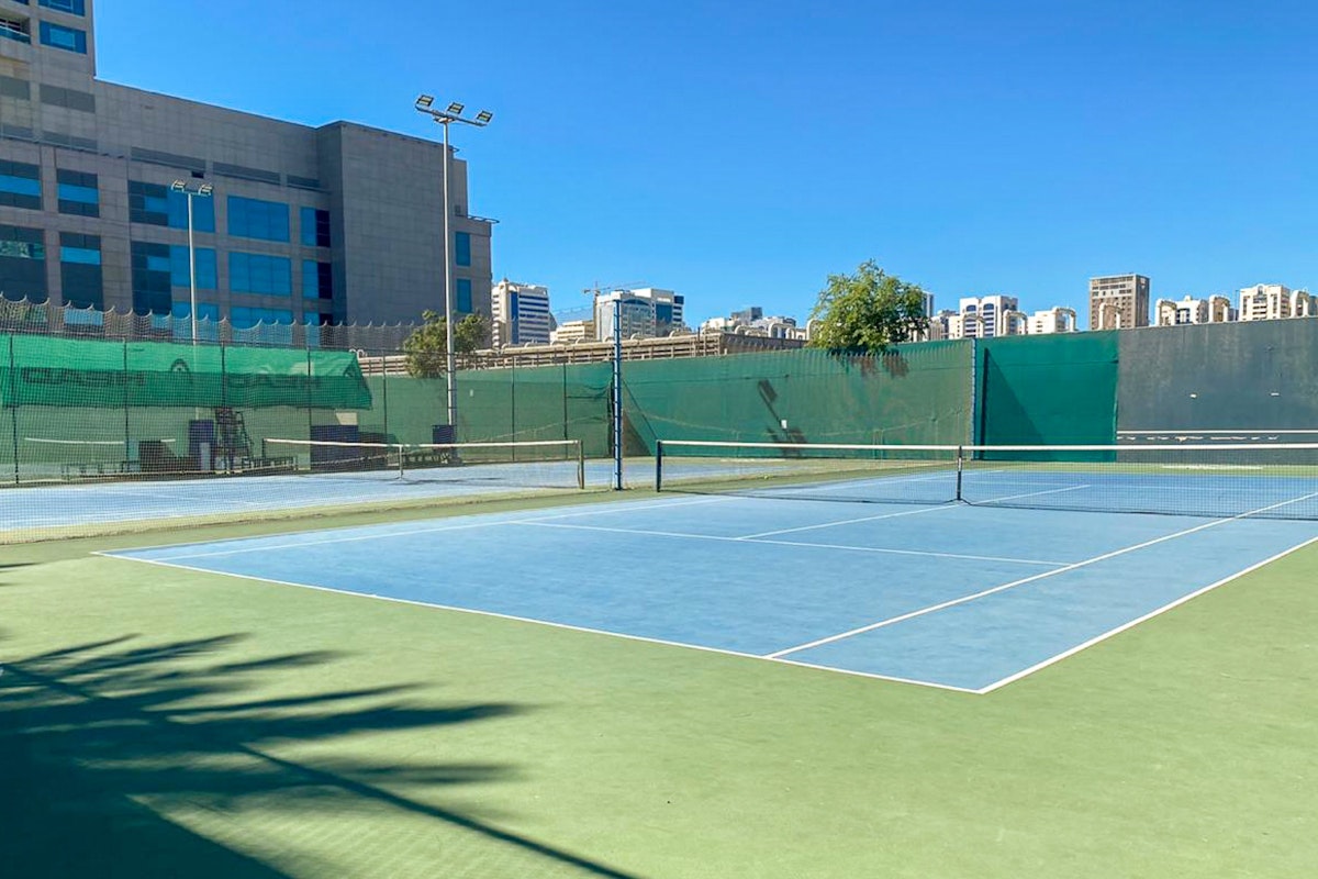 Tennis court with a clear blue sky and city buildings in the background.