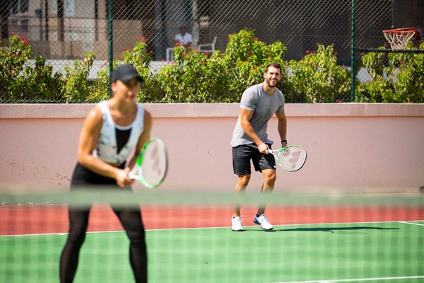 Tennis and squash courts available on Privilee A man and woman are playing tennis together on a court, smiling and having fun while getting ready to return the ball.