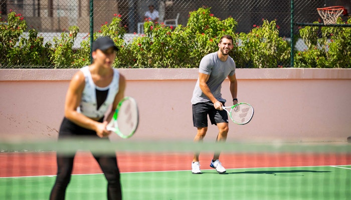 Tennis and squash courts available on Privilee A man and woman are playing tennis together on a court, smiling and having fun while getting ready to return the ball.
