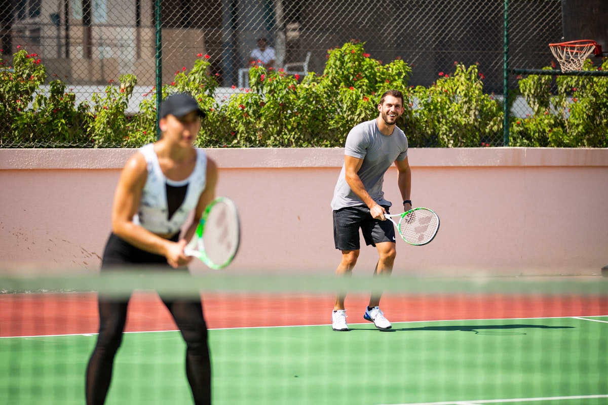A man and woman are playing tennis together on a court, smiling and having fun while getting ready to return the ball.