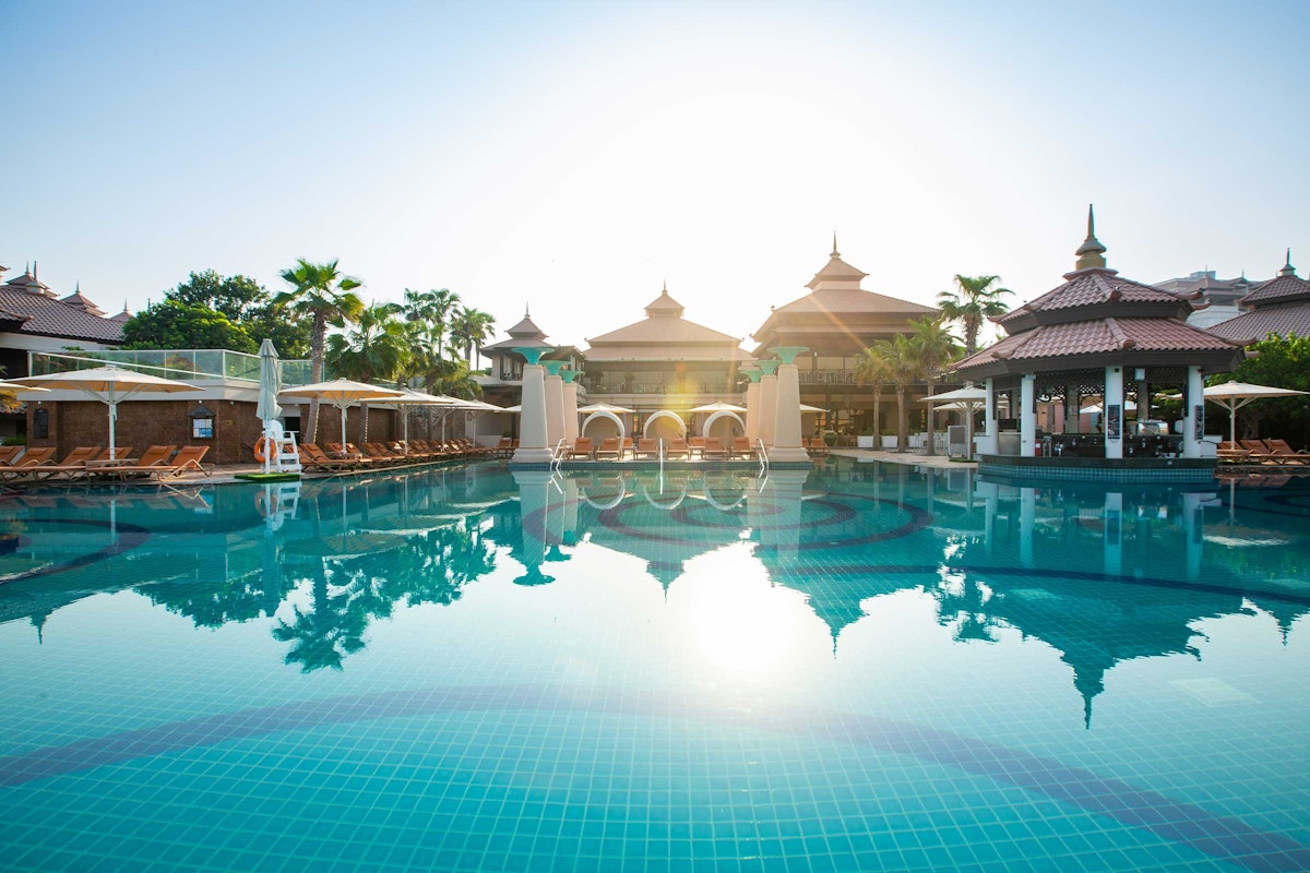 Serene pool with reflections and traditional-style buildings in the background.