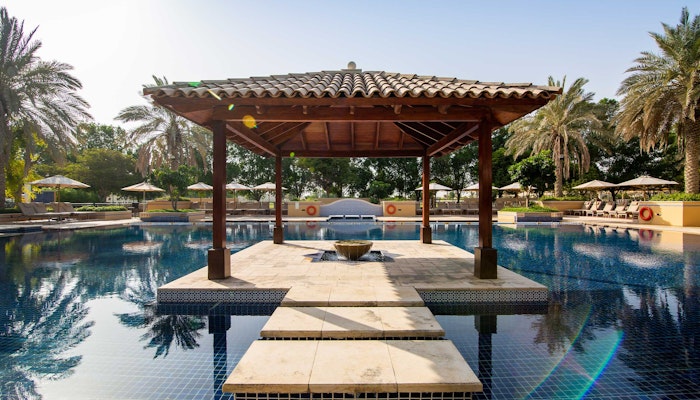Dubai Polo & Equestrian Club Outdoor pool with a wooden pavilion in the center, surrounded by palm trees