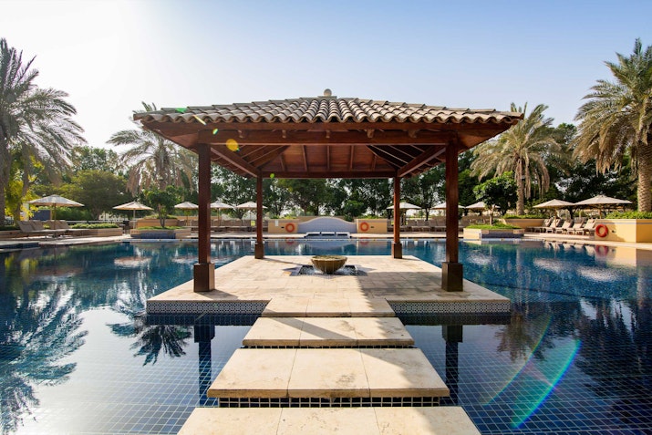 Outdoor pool with a wooden pavilion in the center, surrounded by palm trees