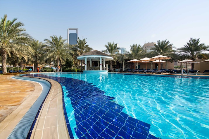 Bright blue pool with curved tile design and palm trees in the background