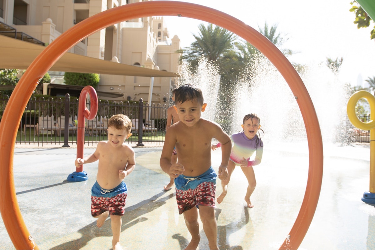 Fairmont The Palm Children running through a colorful water play area with fountains and arches.
