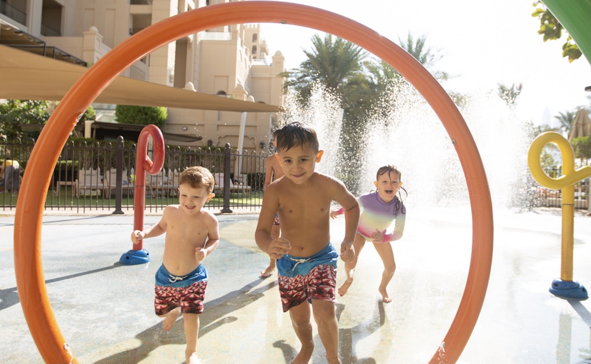 Children running through a colorful water play area with fountains and arches.