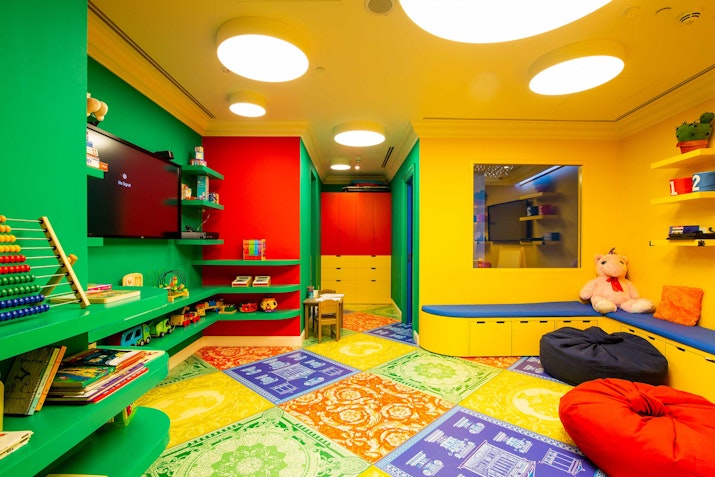 Brightly colored children's playroom with bookshelves, soft seating, and toys.