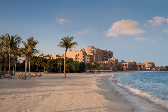 Beachfront view of a resort with palm trees at sunset.