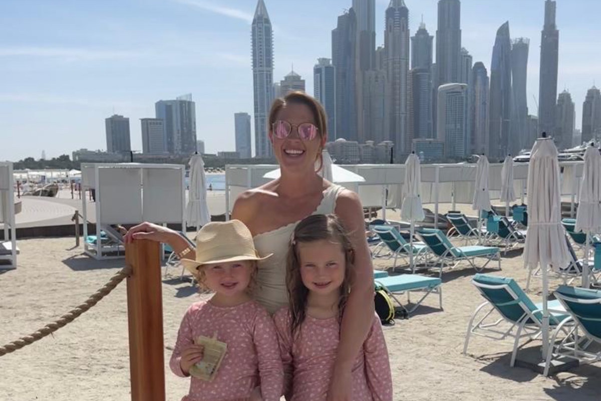 Family of three posing together outdoors with a city skyline and beach chairs in the background
