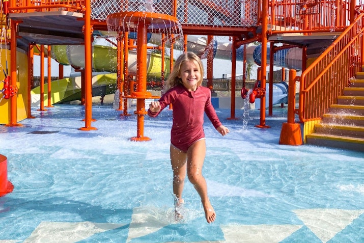 Child running through a water play area with colorful slides in the background