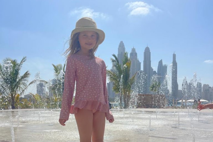 Young girl smiling and standing in a water fountain with the city skyline in the background