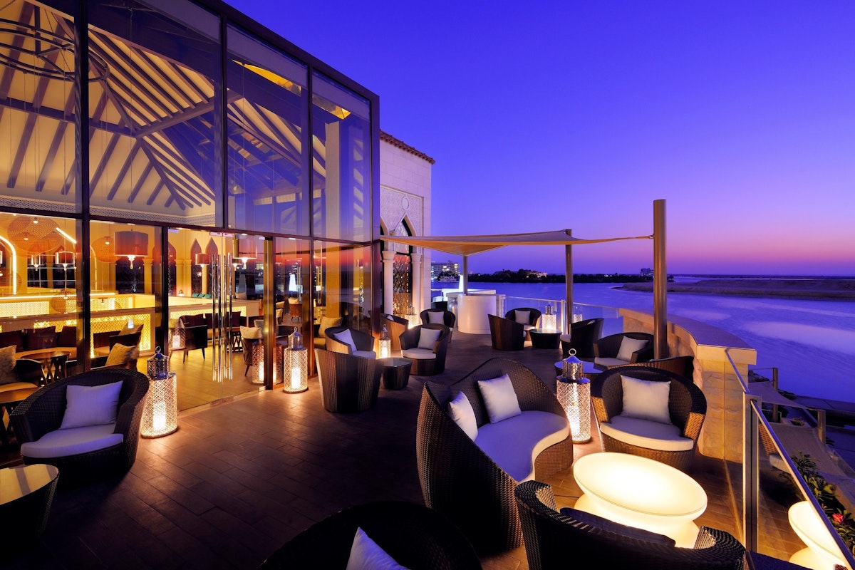 A stylish outdoor lounge area at sunset with modern seating and warm lighting, offering views of the ocean and a clear sky