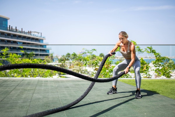 Woman using battle ropes in an outdoor fitness area.