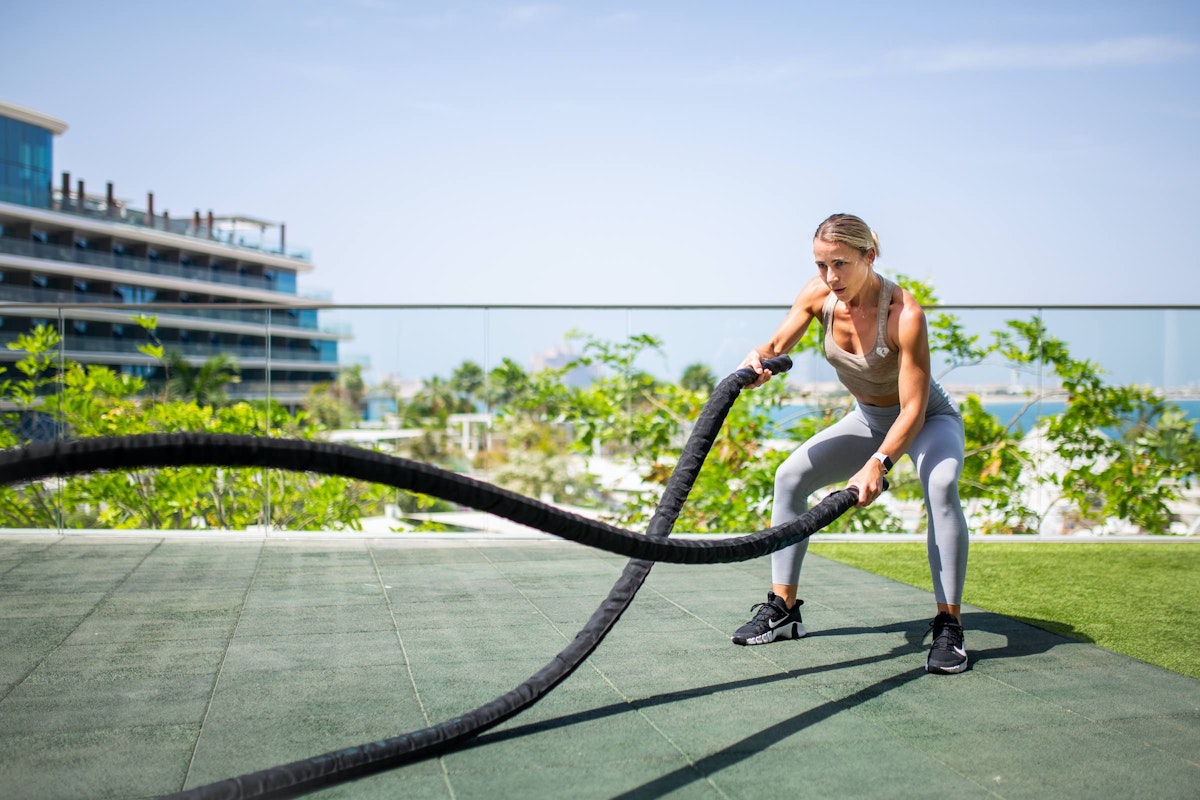 Woman using battle ropes in an outdoor fitness area.