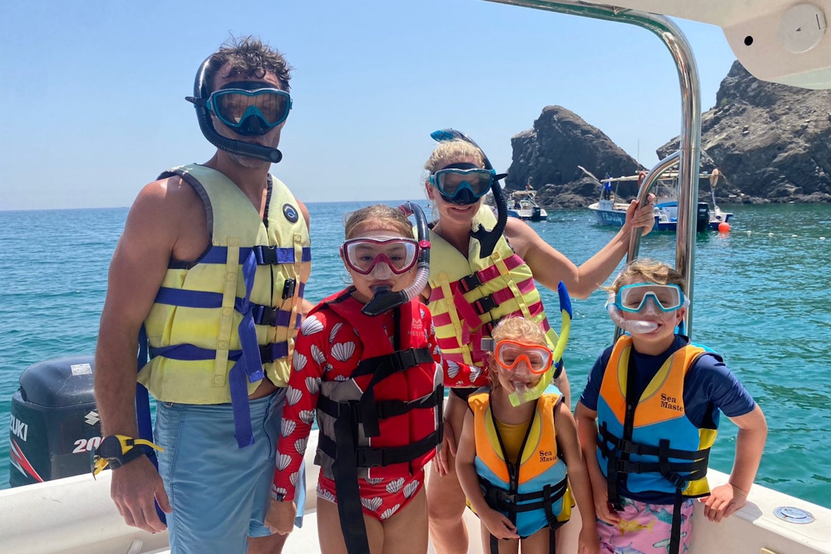 A family of five wearing life jackets and snorkels on a boat in the sea.