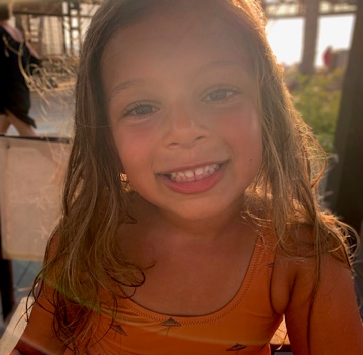 JA The Resort A smiling young girl with long hair, wearing an orange dress, captured in sunlight