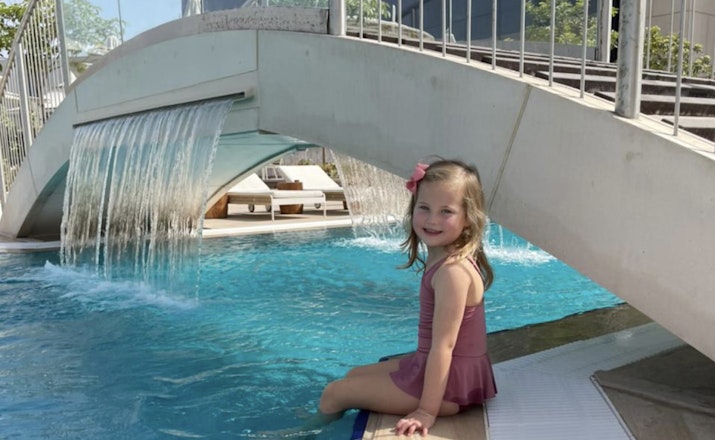 Young girl sitting near a pool under a waterfall.