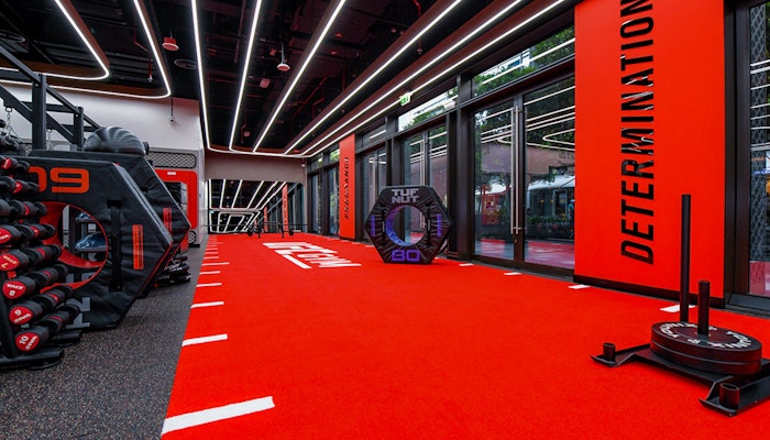 Push your limits in a space designed for strength and functional training An intense fitness area with bright red flooring, motivational words like 'DETERMINATION' on the walls, weights and fitness equipment, all set under bright lights