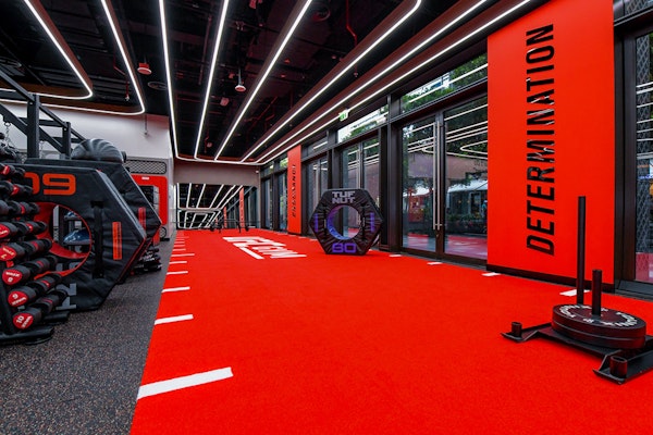 An intense fitness area with bright red flooring, motivational words like 'DETERMINATION' on the walls, weights and fitness equipment, all set under bright lights