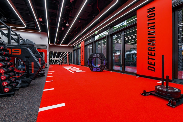 An intense fitness area with bright red flooring, motivational words like 'DETERMINATION' on the walls, weights and fitness equipment, all set under bright lights