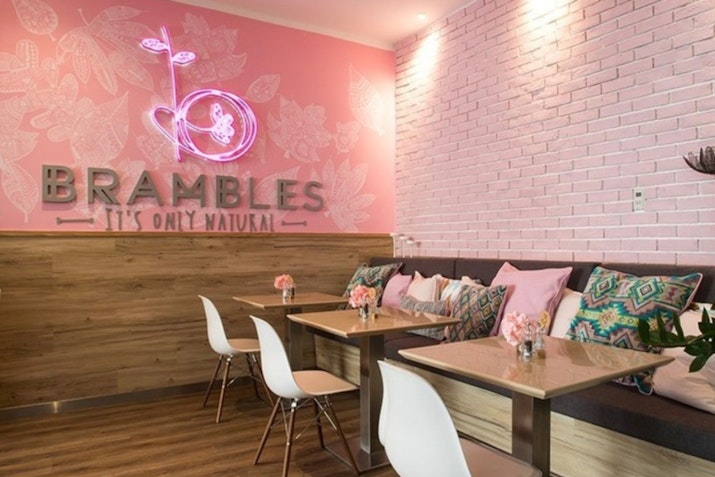 Brambles Interior of a café with pink walls, neon sign, and cozy seating.