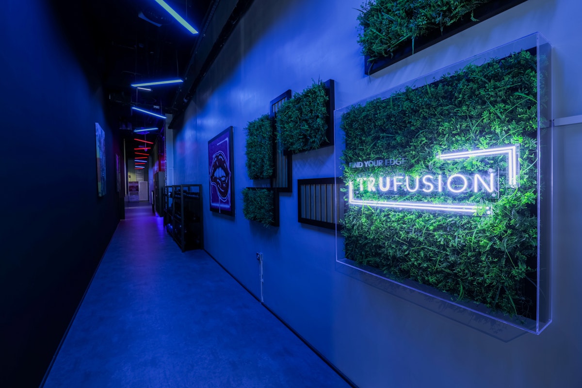 TruFusion Dubai A modern hallway with neon blue lighting and greenery accents, featuring a prominent "Trufusion" sign on the wall.