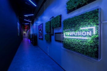 A modern hallway with neon blue lighting and greenery accents, featuring a prominent "Trufusion" sign on the wall.