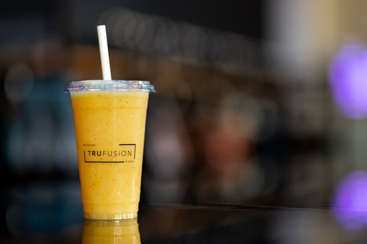 A smoothie in a clear cup with a logo, placed on a counter, with a blurred background.
