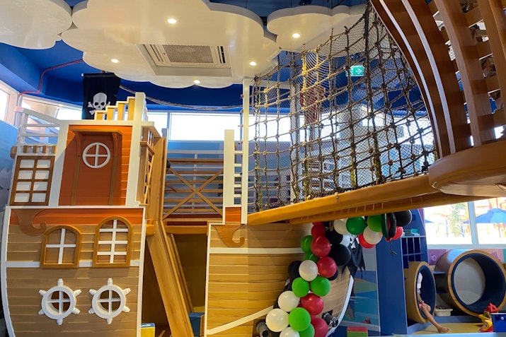 Pirates and Mermaids Kids’ Club An indoor playground designed like a pirate ship, featuring a climbing structure, netting, and colorful decorations.
