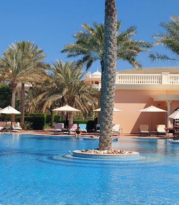 Kempinski Hotel and Residences Palm Jumeirah A tranquil pool surrounded by palm trees and lounge chairs on a sunny day.