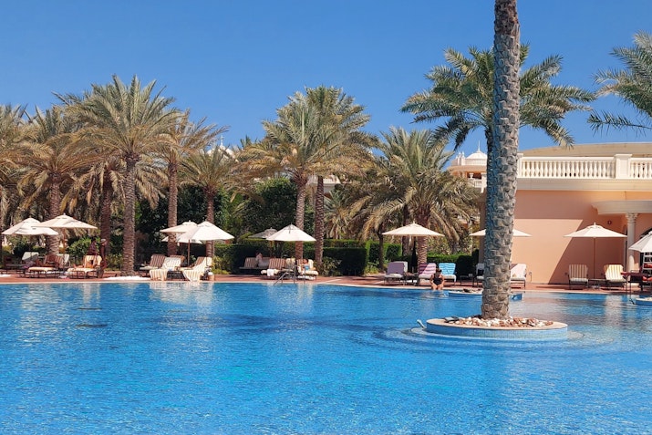 A tranquil pool surrounded by palm trees and lounge chairs on a sunny day.
