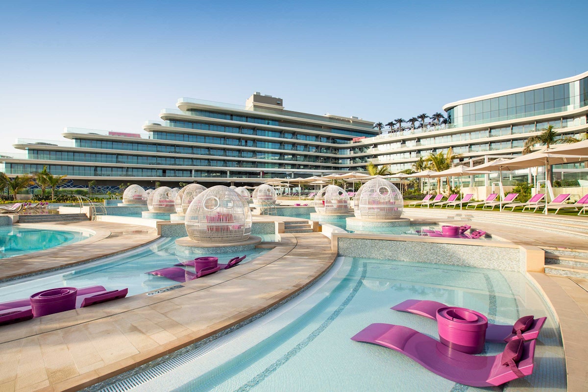 The W Dubai Palm Jumeirah A luxurious pool area with modern purple lounge chairs and bubble-shaped pods, adjacent to a sleek hotel building.