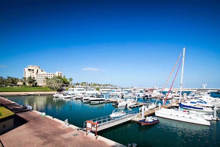 JA The Resort A marina filled with various boats and yachts, with a clear blue sky overhead and a hotel visible in the background