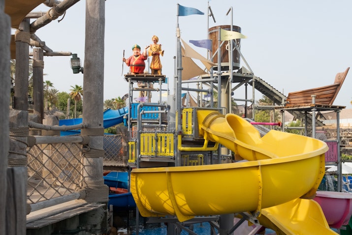 Children's play area with a bright yellow slide, water play structures, and colorful decor at a water park