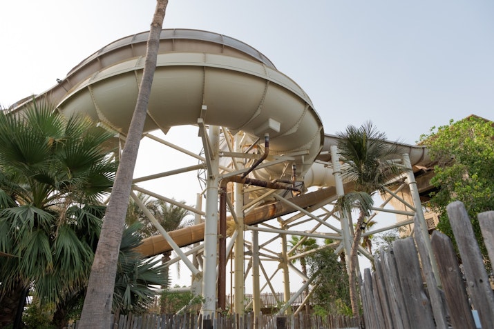 Large circular water slide structure surrounded by tropical palm trees and a rustic wooden fence