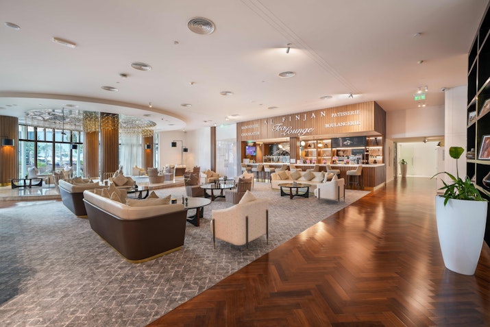 A stylish, modern hotel lounge with comfortable seating, elegant decor, and a bar area, featuring soft lighting and wooden flooring.