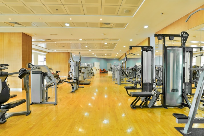 Spacious gym with various workout machines and wooden flooring.