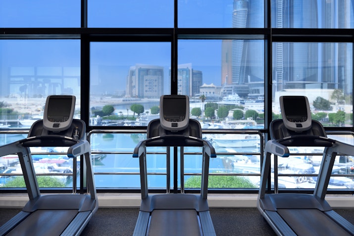 Cardio machines with a scenic view of a marina through large windows.