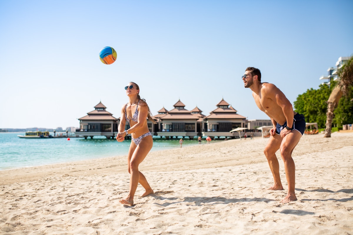 Couple playing beach volleyball on a sandy beach with a tropical backdrop.