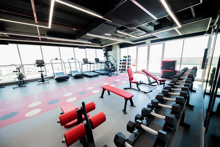 A well-lit gym with various exercise equipment, including treadmills, dumbbells, and weight benches.