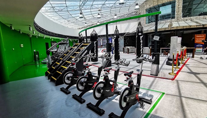 Adrenagy A spacious gym with various exercise equipment, including stationary bikes, stair climbers, and punching bags, all set under a glass ceiling.