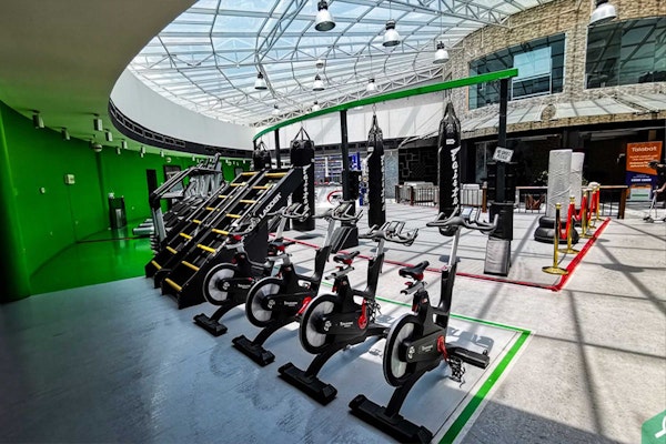 A spacious gym with various exercise equipment, including stationary bikes, stair climbers, and punching bags, all set under a glass ceiling.