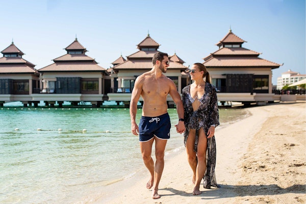 Couple walking on beach near overwater bungalows.